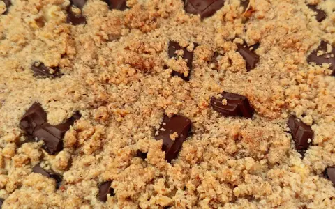 Gros plan sur un délicieux crumble pomme amande parsemé de morceaux de chocolat noir fondants.