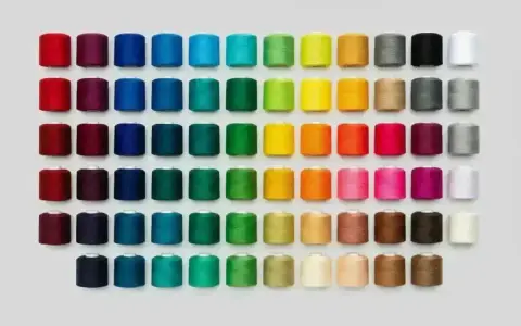 Una gran variedad de tipos de hilos de coser en carretes, organizados por color en filas y columnas.