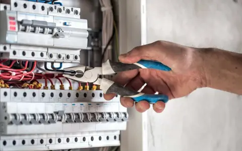 Elektryk pracuje przy skrzynce z bezpiecznikami. Gdy zgłosić brak prądu, warto sprawdzić właśnie takie instalacje.