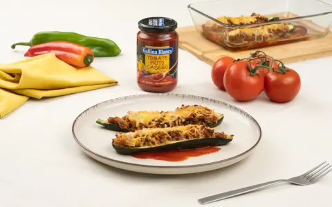 Dos calabacines rellenos de carne y gratinados con queso, servidos en un plato con tomate frito.