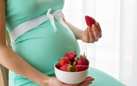 Pancione e fragole, un dolce desiderio in gravidanza. La futura mamma tiene una fragola in mano e una ciotola piena.