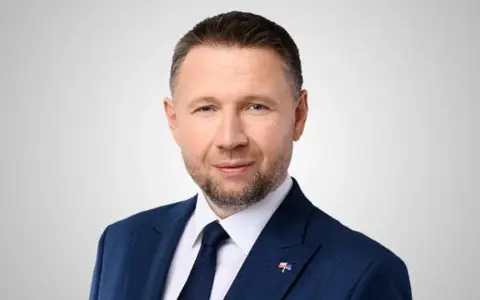 Mężczyzna w granatowym garniturze, z krótkimi włosami i zarostem, to minister spraw wewnętrznych.