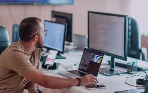 Mężczyzna w okularach pracuje przy komputerze, testując aplikację. To praca testera aplikacji, gdzie sprawdza się działanie oprogramowania.