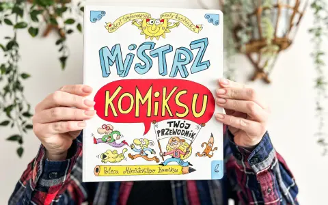 Okładka książki "Mistrz Komiksu" z rysunkami postaci i słońca, trzymana przez ręce.