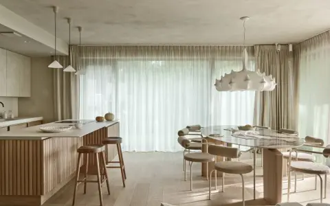 Nowoczesna kuchnia z wyspą i jadalnią. Wnętrze rozświetla designerska lampa wisząca, a całość dopełnia podwieszany sufit.