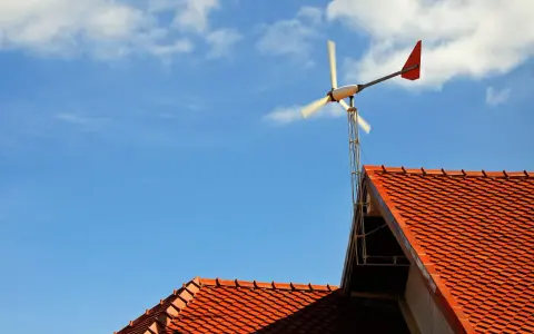 Mała elektrownia przydomowa na tle błękitnego nieba z chmurami. Wirnik turbiny wiatrowej obraca się, dostarczając czystą energię.