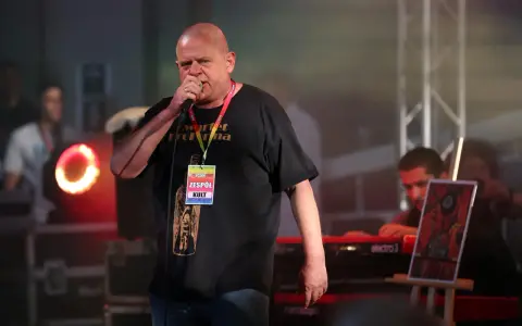 Kazik Staszewski śpiewa na koncercie, ubrany w czarną koszulkę z napisem "Kwartet Pro Forma" i identyfikatorem "Zespół KULT".