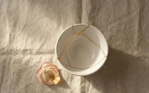 Biała miska z pęknięciami zespolonymi złotem, jak w kintsugi, obok zasuszonego płatka róży. Symbolizuje proces leczenia, jak w przypadku osobowości borderline test.
