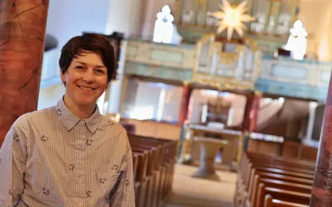 Eine lächelnde evangelische Pfarrerin steht in einer Kirche vor einer Orgel.
