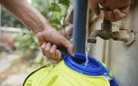 Wasser fließt aus einem alten Wasserhahn in eine gelbe Trinkblase. Nach dem Befüllen muss die Trinkblase trocknen.