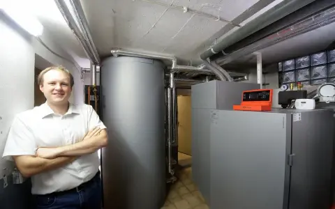 Mann vor Pelletheizung und großem Speicher in Heizungsraum.