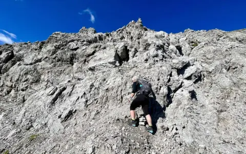 Bergsteigerin klettert über felsiges Gelände, das der UIAA-Skala entspricht. Blauer Himmel und schroffe Felsen.