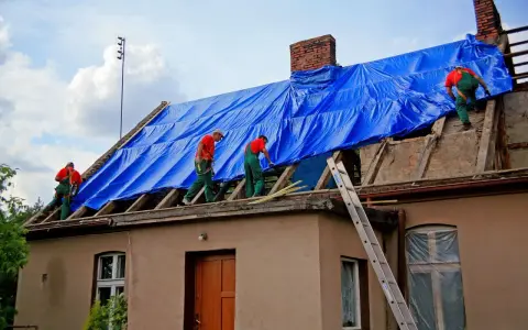 Robotnicy na dachu kryjącym niebieską plandeką. Zastanawiasz się, ile kosztuje pozwolenie na budowę?
