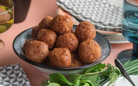 Un piatto colmo di polpette di fagioli dorate, guarnito con erbe fresche.