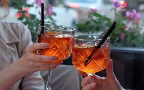 Dwie osoby wznoszą toast Aperolem. Orzeźwiający drink z pomarańczą i truskawką.