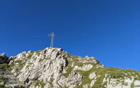 Szczyt Giewontu z krzyżem i błękitnym niebem. Trasa wspinaczkowa jest stroma i kamienista.