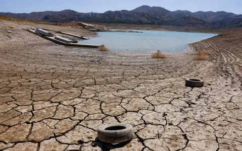 Seca tierra agrietada con un lago bajo y barcos varados. Neumáticos abandonados sugieren una contaminación natural y humana.