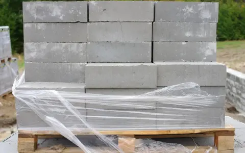 Stos betonowych bloczków fundamentowych na palecie, owiniętych folią.