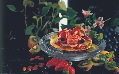 Eine süße Pizza mit Eis, Beeren und Kiwi. Mandeln und Trauben garnieren das Dessert.