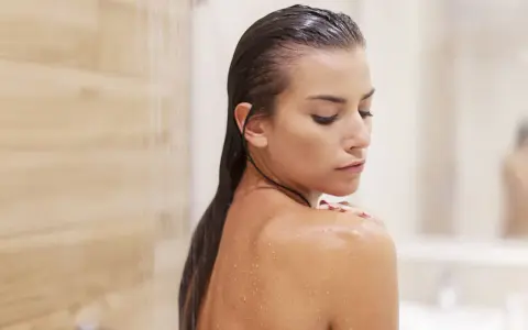 Mujer en la ducha, con gotas de agua en su piel. Pregúntate cada cuanto exfoliar el cuerpo para una piel radiante.