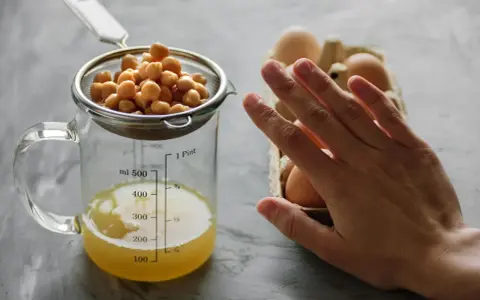 Kichererbsen im Sieb über Messbecher mit Aquafaba. Eier im Hintergrund. Perfekt für ei ersatz backen.