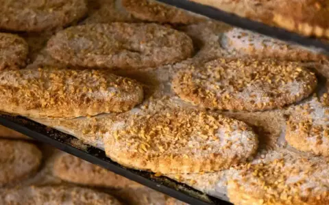 Varias cocas de llardons recién horneadas, cubiertas de azúcar y trocitos de frutos secos, listas para disfrutar.