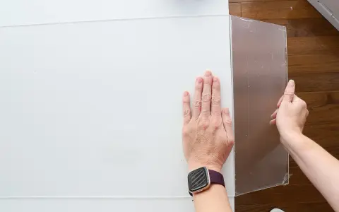 Hands guide a scoring tool along a white acrylic sheet, demonstrating how to cut acrylic sheet for a project.