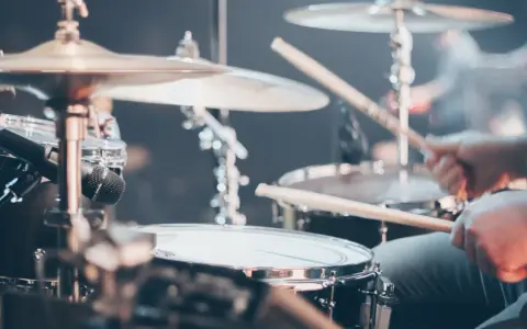 Gros plan sur un set de batterie, avec des baguettes en action. Différents types de tambour et cymbales sont visibles.