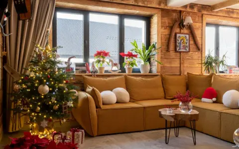 Przytulny salon z choinką i prezentami, tworzący atmosferę **świąt w górach**. Drewniane ściany i okna dodają uroku.
