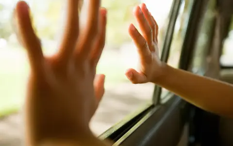 Dziecko z podwrażliwością dotykową delikatnie dotyka szyby samochodu, czując świat za nią.