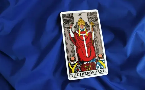 Karta Tarota "The Hierophant" na niebieskim tle. Postać w czerwonych szatach z tiarą i krzyżem.