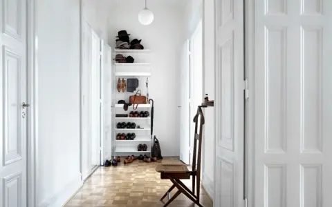 Ein heller, schmaler Flur wirkt optisch breiter durch weiße Türen und eine offene Regalwand mit Schuhen und Accessoires.