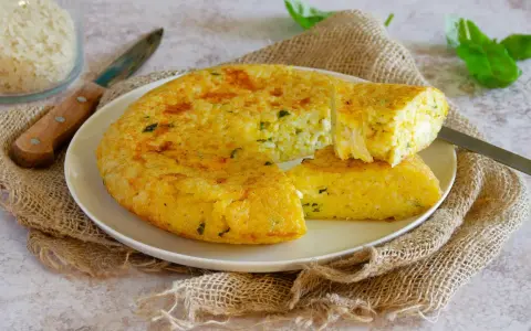 Una gustosa frittata di riso dorata, con erbe aromatiche, servita su un piatto bianco con una fetta tagliata.
