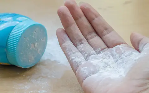 Mano con borotalco bianco sparso, vicino al contenitore blu. Attenzione: il borotalco è cancerogeno.
