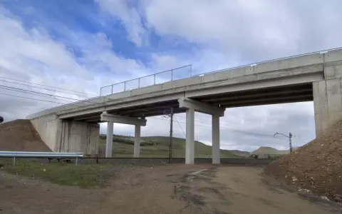Un puente de hormigón cruza vías de tren. Los pilares de soporte, que son un estribo, sostienen la estructura. El cielo está nublado.