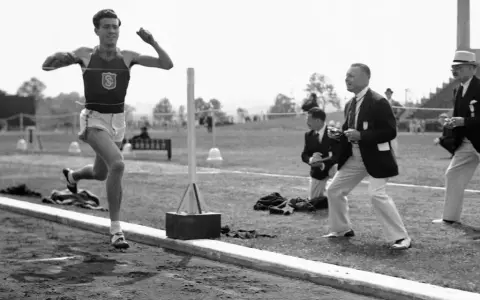Louis Zamperini biegnie na bieżni, podczas gdy sędziowie obserwują zawody.