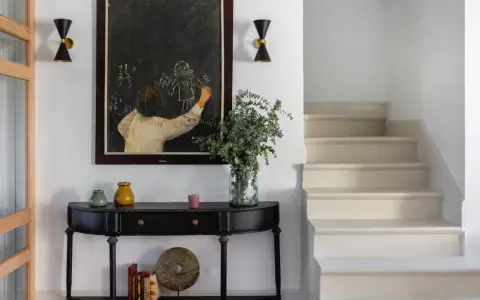 Entrada de una casa pequeña con consola negra, cuadro de tiza y escaleras. Un toque de feng shui casa pequeña para armonizar el espacio.