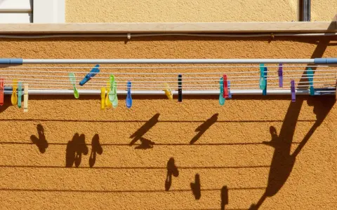 Variados tipos de tendederos exteriores con pinzas de colores sujetan la ropa. Las sombras proyectadas crean un patrón interesante sobre la pared texturizada.