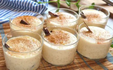 Seis vasitos de cremoso arroz con leche, espolvoreados con canela y decorados con una ramita de canela.