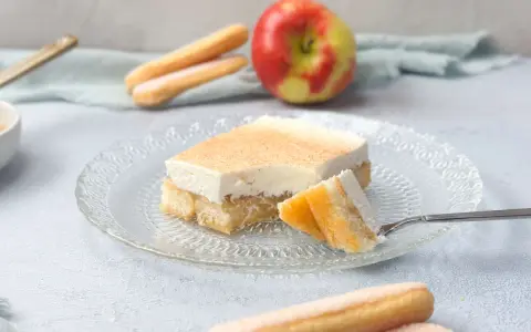 Ein Stück Apfel Schmand Kuchen mit Löffelbiskuits und einem Apfel im Hintergrund.