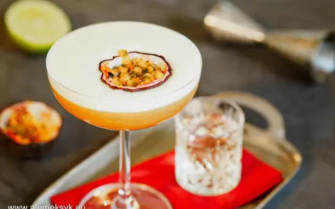 Orzeźwiający drink z martini, ozdobiony połówką marakui, obok kieliszka z wodą i połówki limonki.