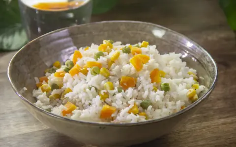 Un tazón de arroz blanco con trozos de zanahoria, guisantes y maíz. Un plato sencillo y colorido de arroz con verduras.