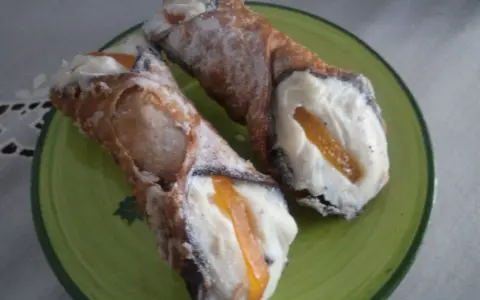 Dwa pyszne cannoli z kremem i kandyzowaną skórką pomarańczową, posypane cukrem pudrem. Ten makaron to prawdziwa rozkosz!
