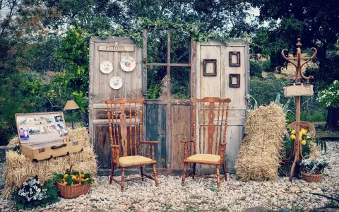 Un rústico photocall boda casero con puertas antiguas, sillas de madera, balas de heno y detalles florales.