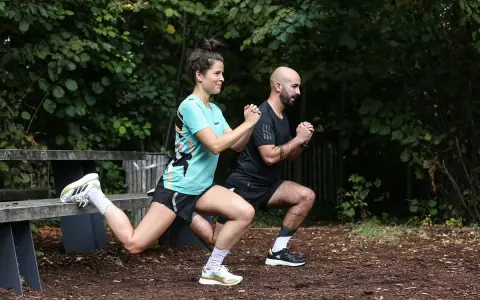 Un couple fait des exercices de renfo course à pied en extérieur, avec des fentes et des squats.