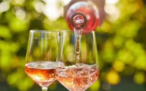 Le danger du vin rosé : une bouteille verse son contenu dans deux verres, créant une cascade pétillante sous un soleil radieux.