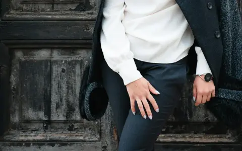 Elegancki facet w sukience, w białej bluzce i czarnych spodniach, stoi przy zniszczonych drzwiach.