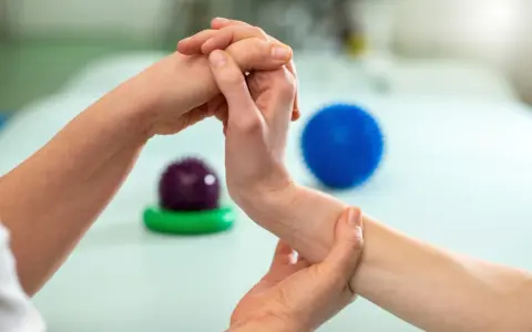 Fizjoterapeuta pomaga pacjentowi w ćwiczeniach na palec trzaskający, używając masażu i piłeczek do rehabilitacji.