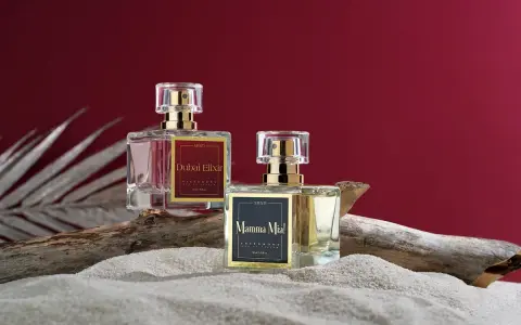 Dwa flakony perfum z etykietami "Dubai Elixir" i "Mamma Mia!", zawierające feromony damskie, stoją na piasku obok kawałka drewna.