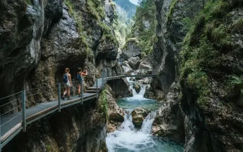 Due escursioniste attraversano passerelle metalliche nel suggestivo orrido di Uriezzo, con un fiume impetuoso che scorre tra le rocce.